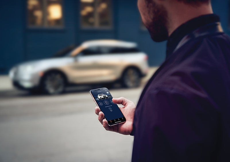 A person is shown interacting with a smartphone to connect to a Lincoln vehicle across the street. | Stivers Lincoln in Waukee IA